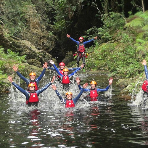 A guided canyoning group splashing in a forest river pool