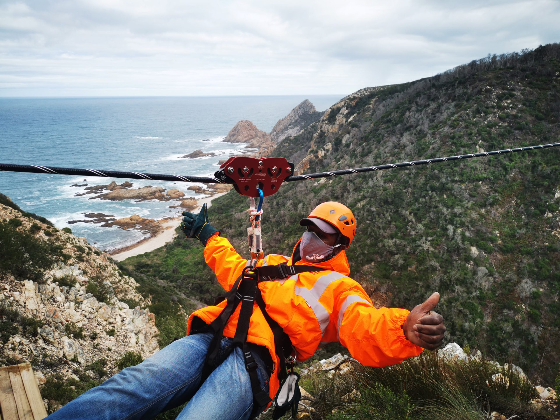 A zipline rider crossing high above the Harkerville coastline