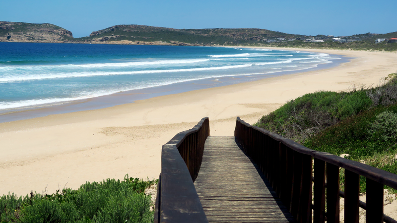Wooden boardwalk opening onto the wide empty sand of Robberg 5 Beach