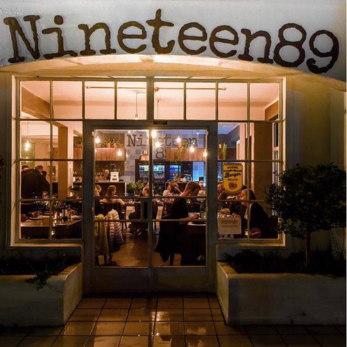 Lit windows and doorway of Nineteen 89 in the evening, diners at tables inside